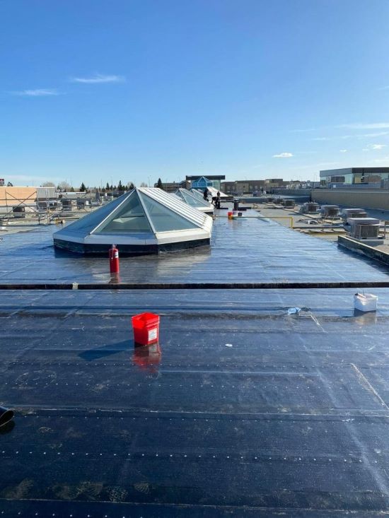 Commercial flat roof with pyramid skylights under clear blue sky.